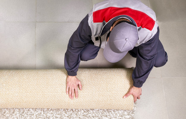 Male Worker Unrolling Carpet On Floor At Home, View From Above 