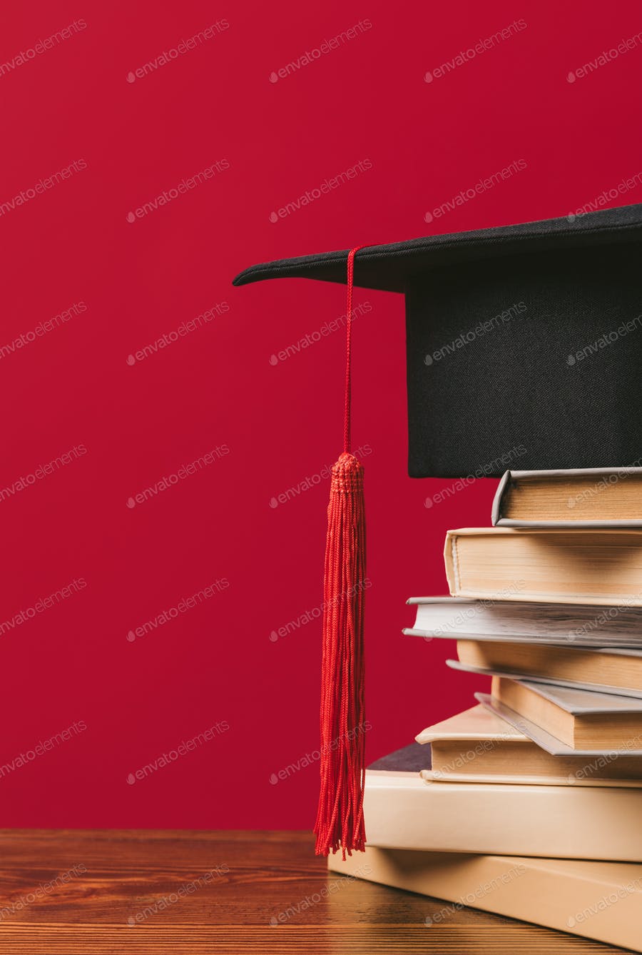 Cropped Image Of Academic Cap On Pile Of Books On Red
