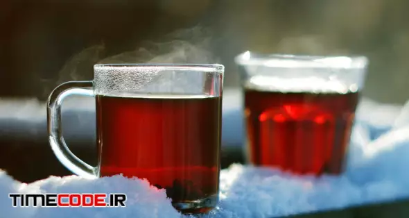Steaming tea in a glass standing on snow at tree branch, closeup shot