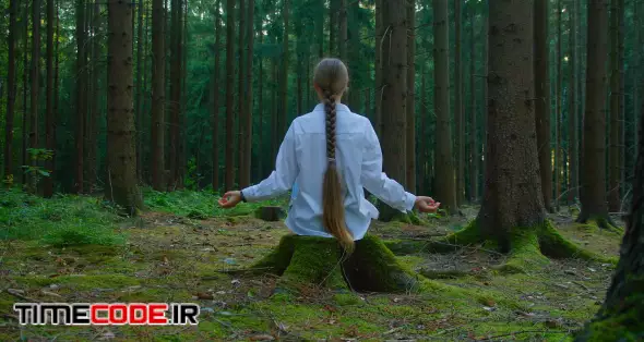 Dark blonde woman meditating in forest. Rear view of long-haired girl sits on green woodland. Self-awareness concept. Slow motion. Healthy lifestyle. Union with nature. 00:12