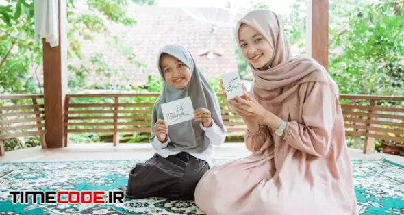 Veiled Asian Mother And Daughter Holding Eid Mubarak Greeting Cards