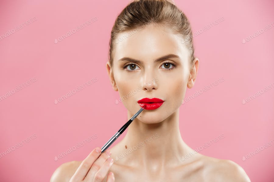 Beauty Concept - Woman Applying Red Lipstick With Pink Studio Background. Beautiful Girl Makes